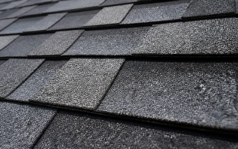 Close-up of slate-grey blended architectural asphalt shingles showing granule texture and dimensional courses.