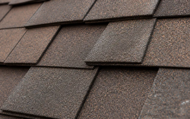 Close-up of weathered-wood brown architectural asphalt shingles showing granule texture and layered tabs.